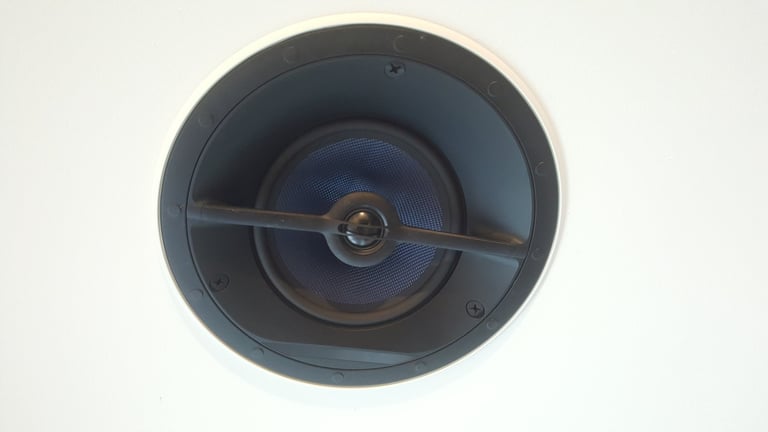 A close-up view of a round, flush-mounted ceiling speaker featuring a blue woven cone and a dark grille, blending seamlessly into a white surface